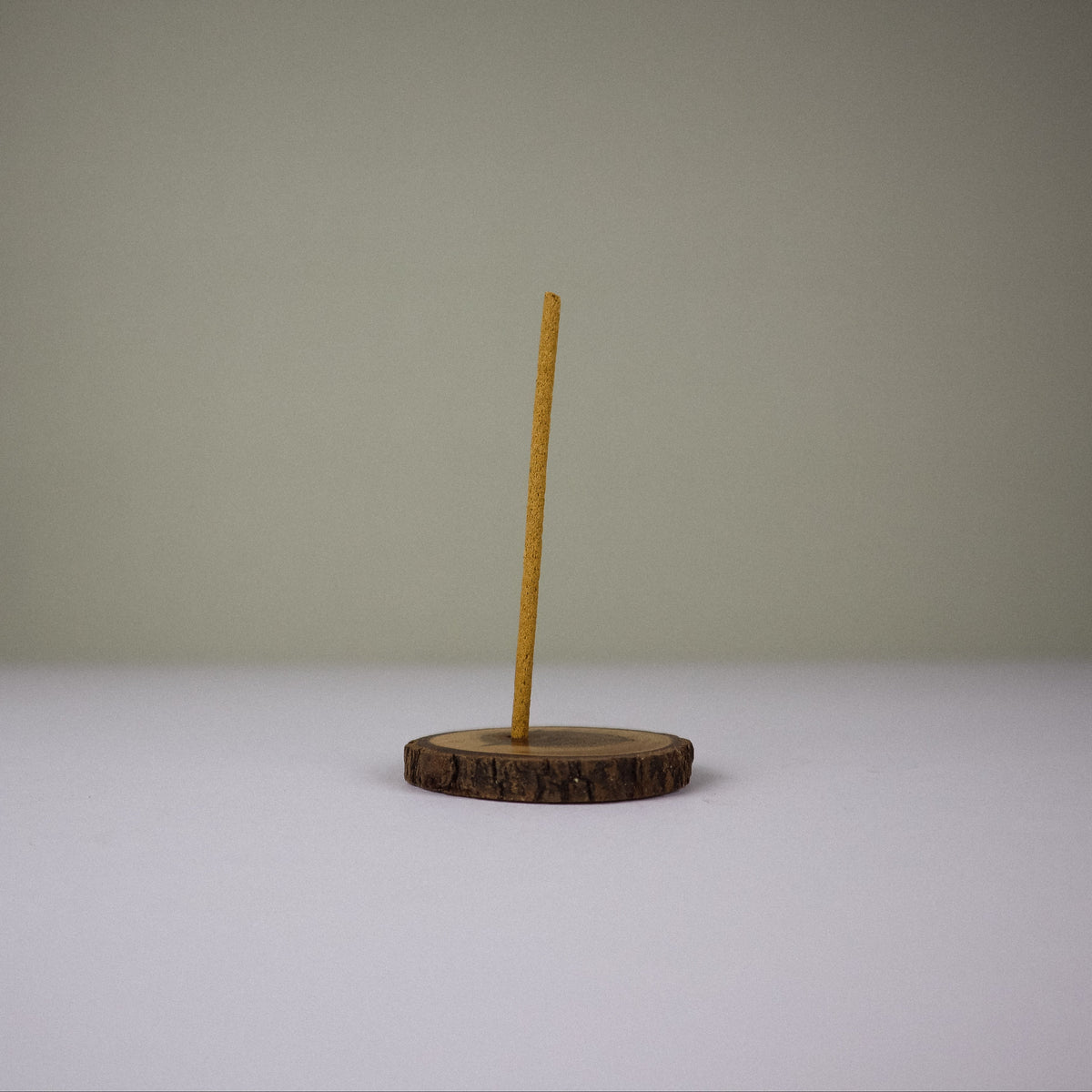 A small wooden stand with a round slice base and a single vertical wooden stick, photographed against a plain light gray background.