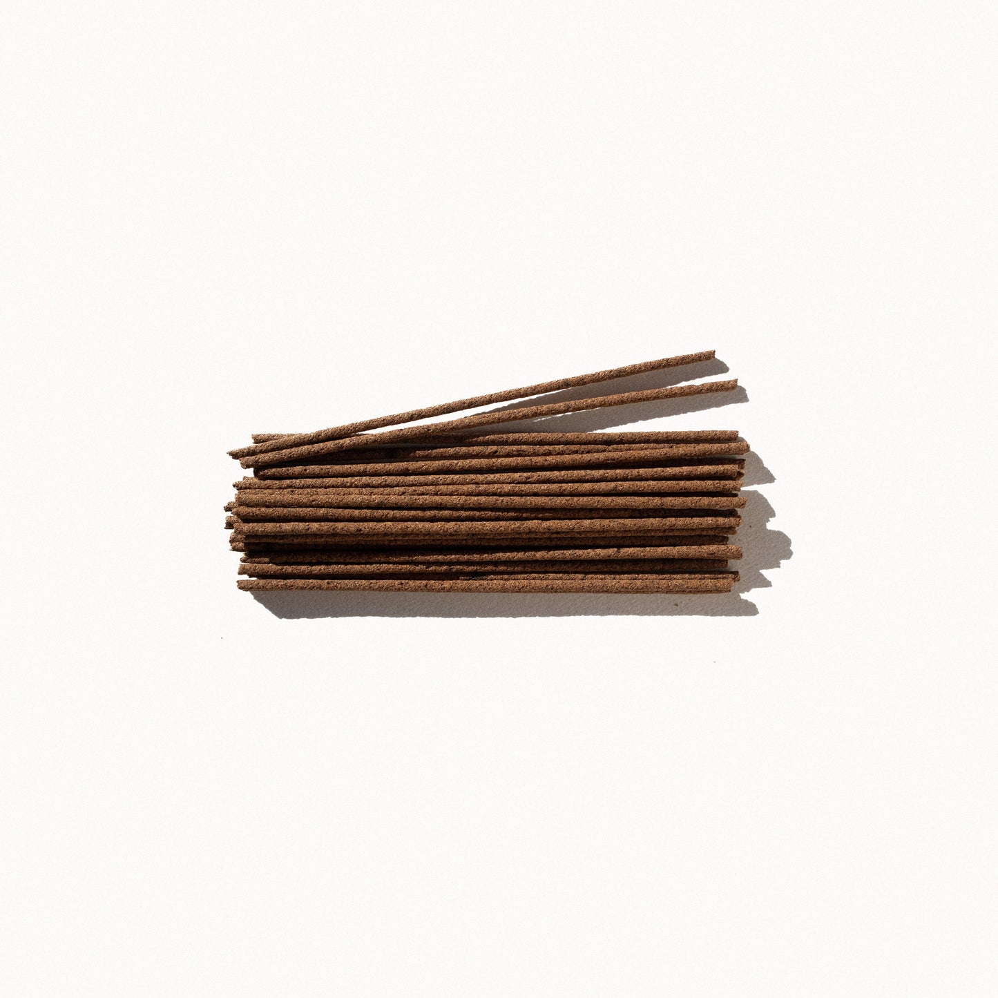 
                  
                    A small pile of brown incense sticks on a plain background.
                  
                