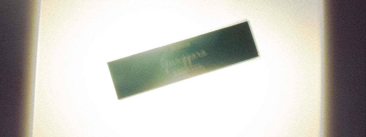 A rectangular dark green blurred box, shown at an angle against a bright, overexposed cream-colored background with dark vignette borders on the sides.